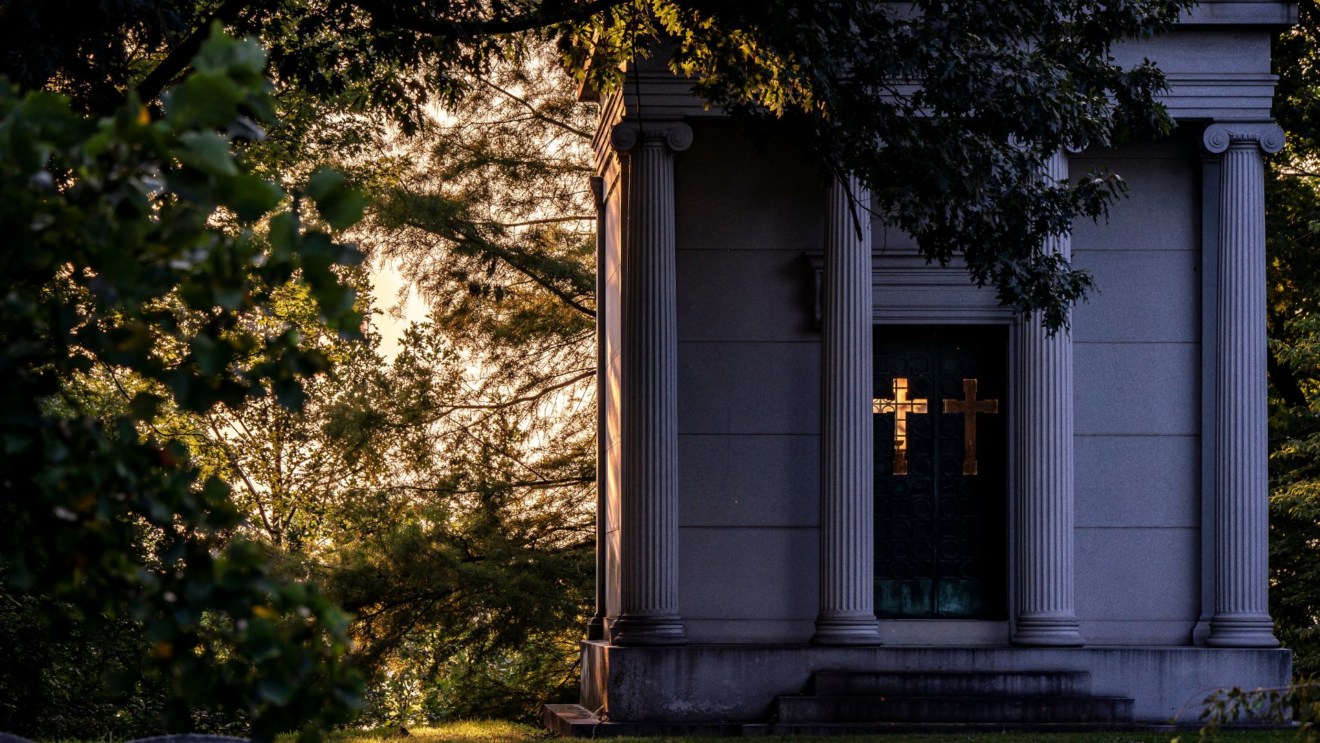 The sun shines through a cut-out cross in this mausoleum.
