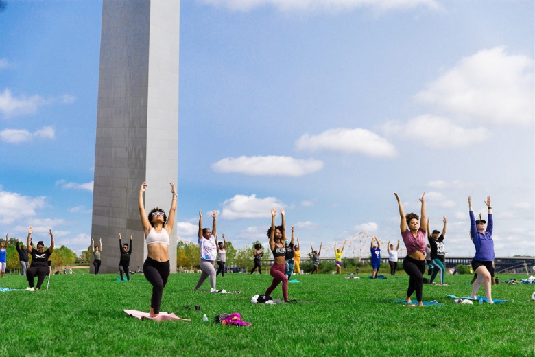 A group enjoys yoga in the sunshine at Gateway Arch National Park.