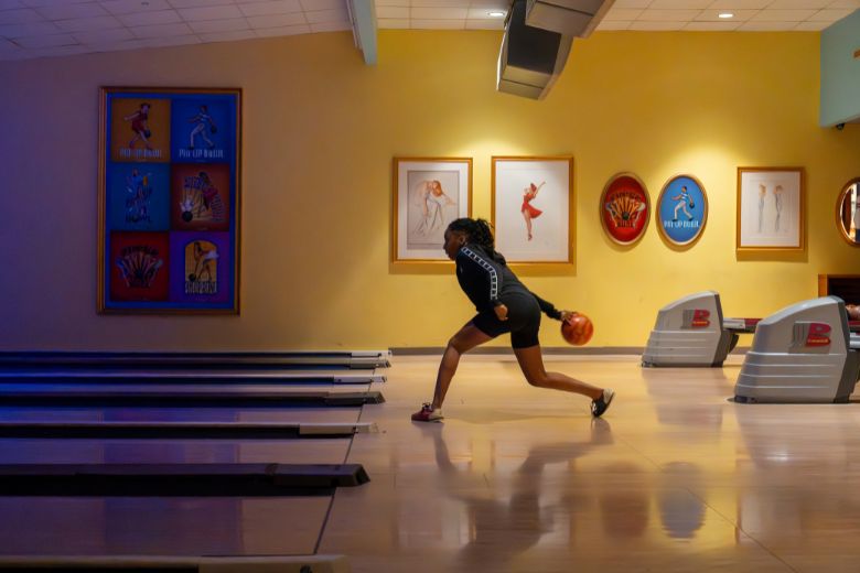 A teenage girl bowls with pin-up girl memorabilia in the background.