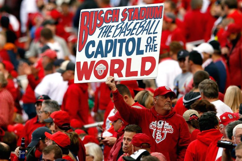 A St. Louis Cardinals fan holds a sign that says, "Busch Stadium: The Baseball Capitol of the World."