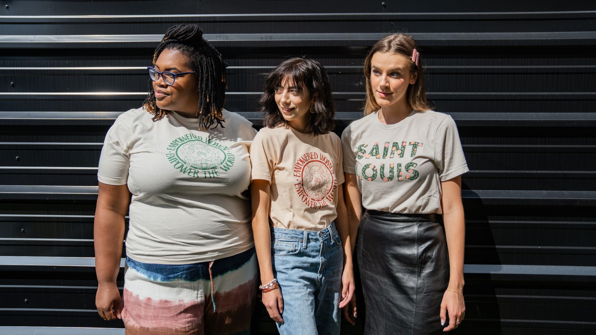 Three women pose in shirts from Procure, a storefront at City Foundry STL that supports small, woman-owned brands.