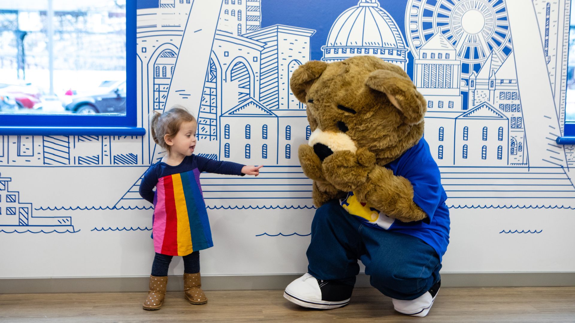 A young girl interacts with an oversized teddy bear at Build-A-Bear Workshop.