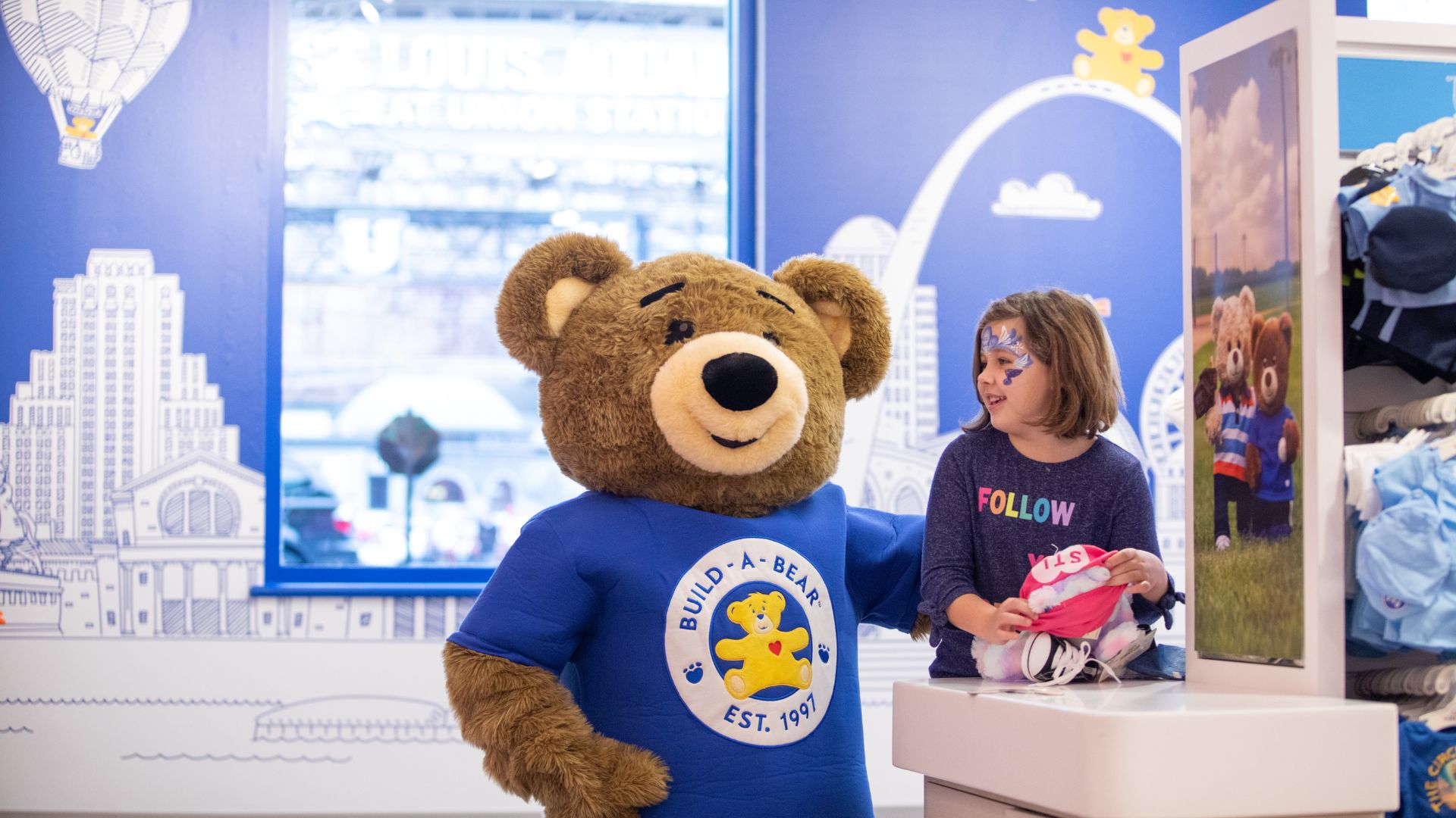 An oversized teddy bear makes a girl laugh at Build-A-Bear Workshop.