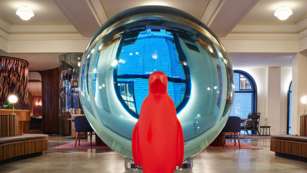 An iconic orange Cracking Art penguin poses in front of Serkan Ozkaya's clear orb in the lobby of 21c Museum Hotel St. Louis.