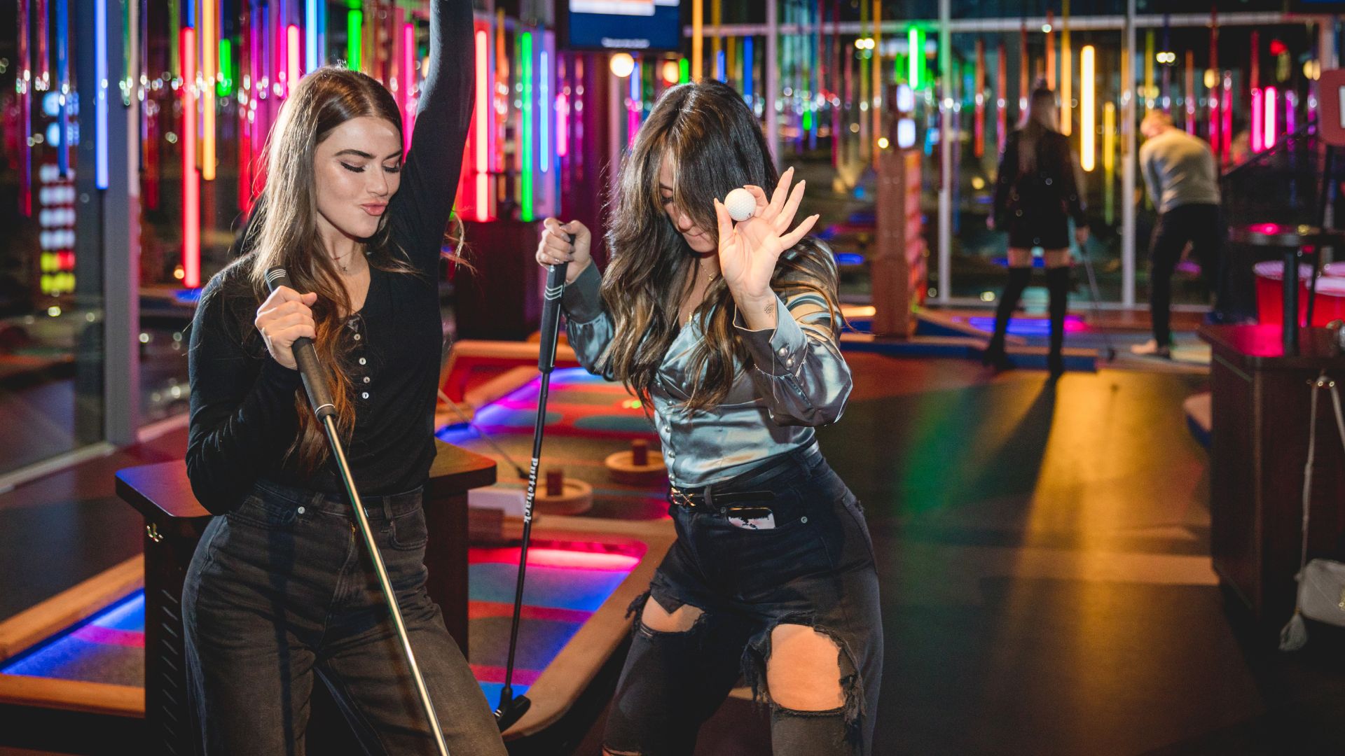 Two girls dance at Puttshack, a tech-infused mini golf course with colorful nightlife vibes.