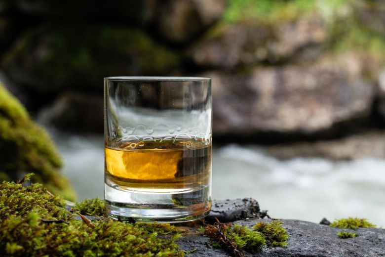 A glass of Irish whiskey sits on a mossy rock.