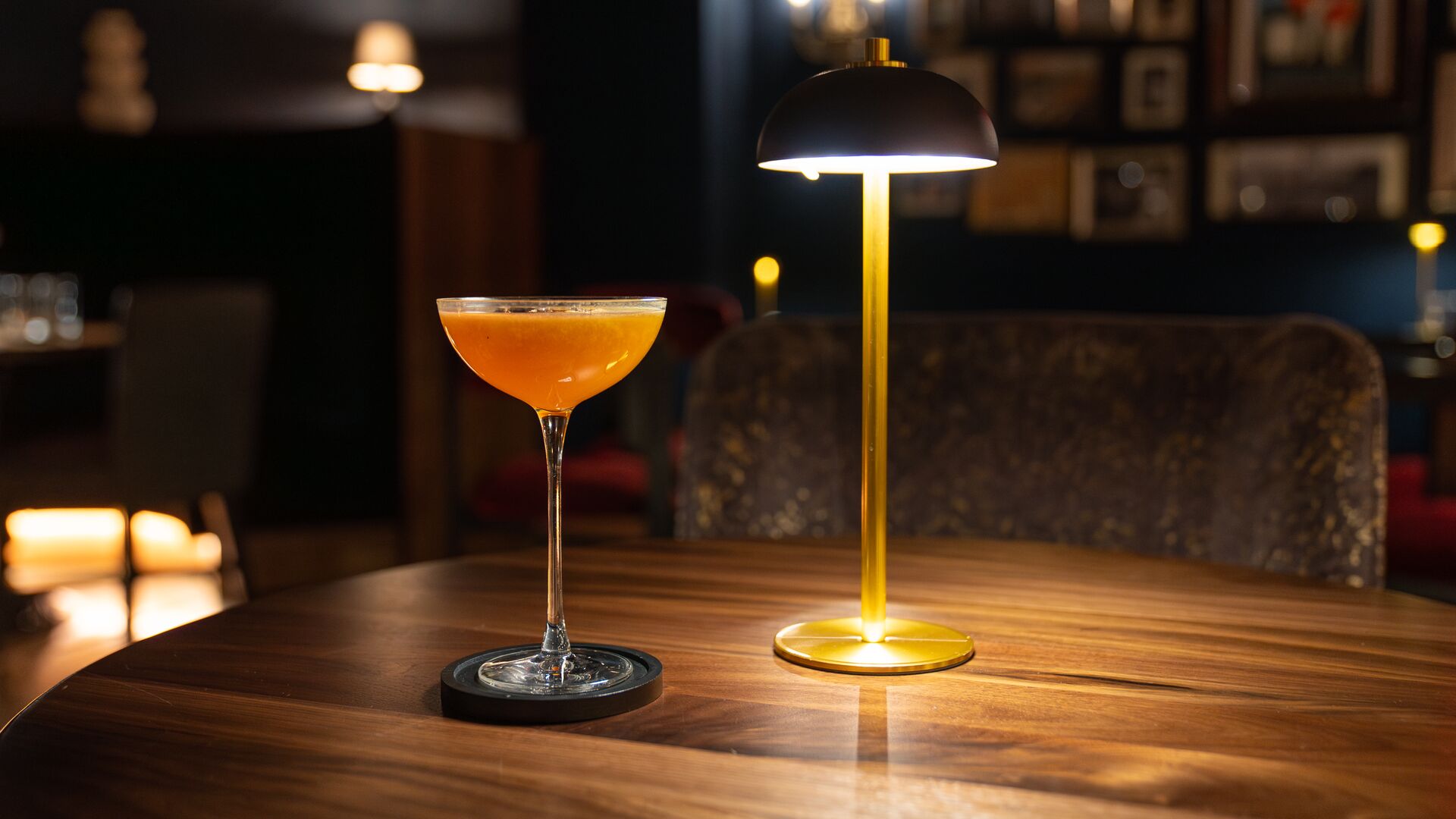 An orange-hued cocktail sits beneath a table lamp.