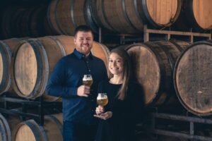 Cory and Karen King, owners of Side Project Brewing, pose in front of barrels in The Cellar.