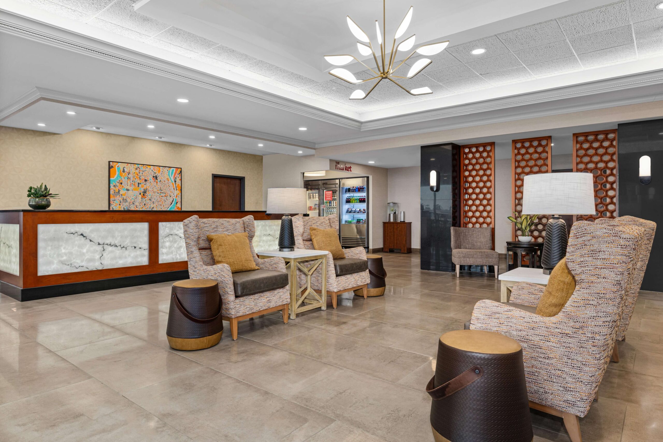 Welcoming hotel lobby featuring a warm wood front desk, comfortable armchair seating, and a convenient grab-and-go market at Drury Inn & Suites St. Louis Creve Coeur.