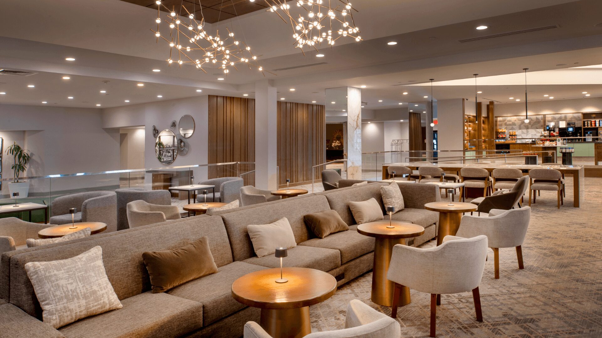 Modern hotel lobby at Hilton St. Louis Airport featuring contemporary light fixtures, comfortable gray sofa seating, and warm wood-paneled walls.