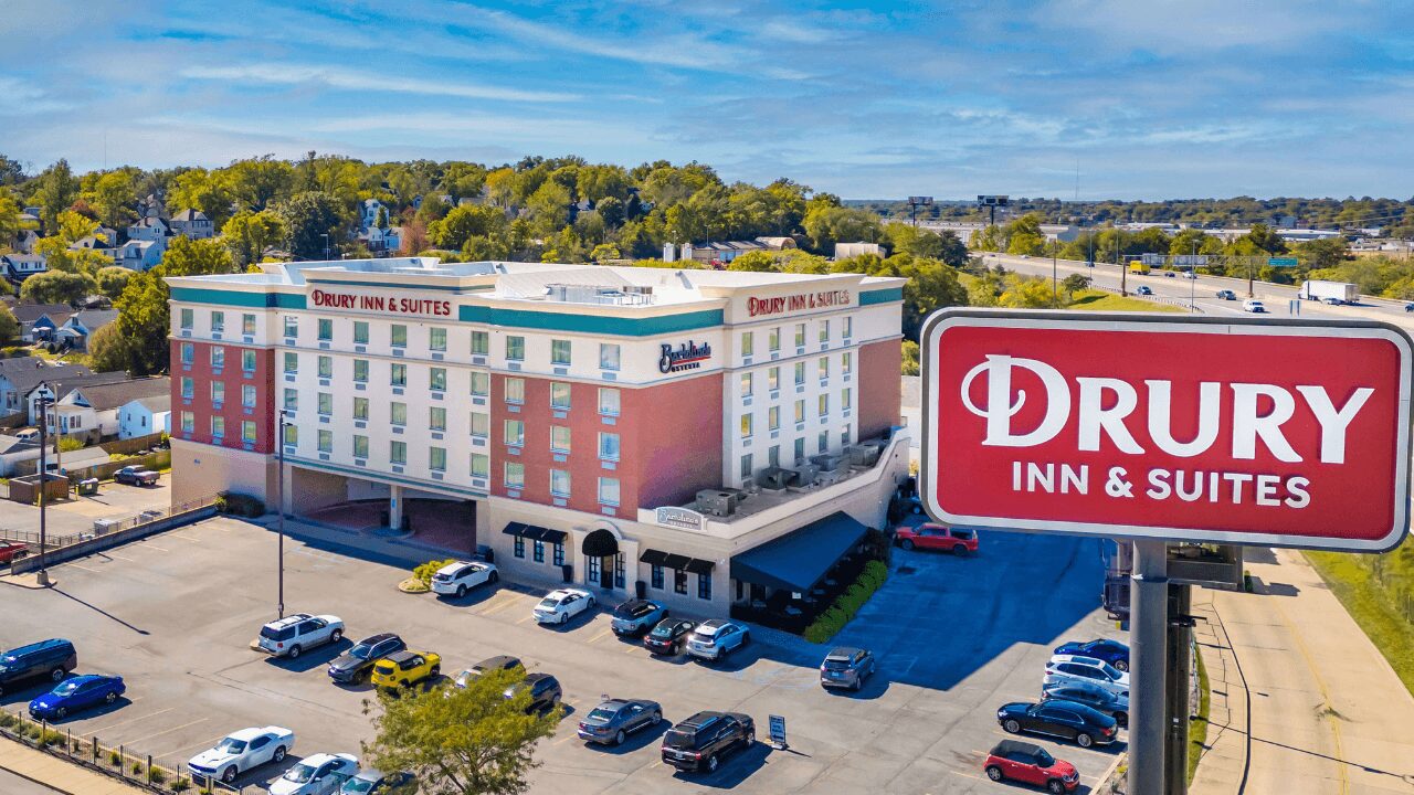 Aerial view of Drury Inn & Suites St. Louis Forest Park showcasing the multi-story hotel, a large roadside marquee sign, ample guest parking, and convenient nearby highway access.