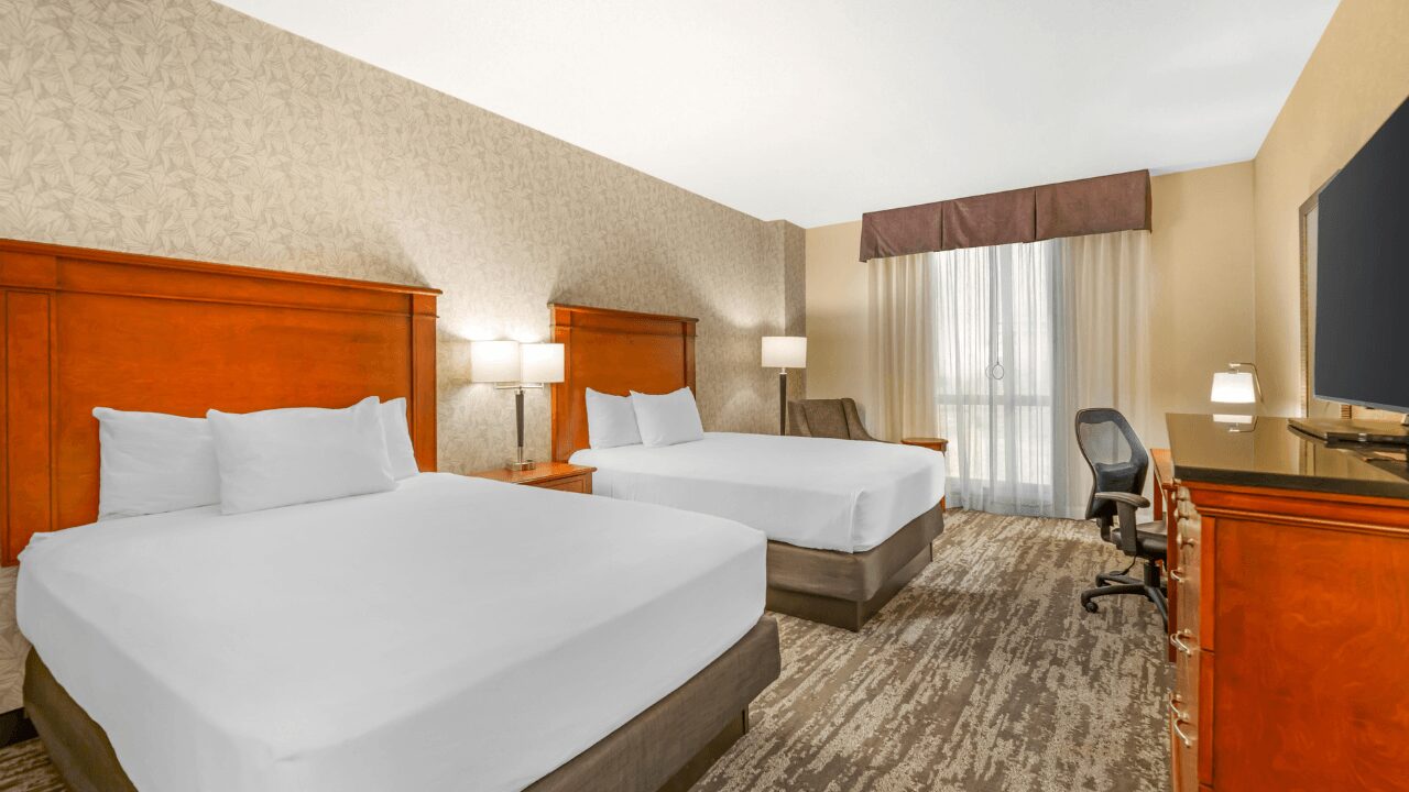 Inviting guest room featuring two queen-sized beds with crisp white linens, a comfortable reading armchair, and a dedicated workspace with an ergonomic chair at Drury Plaza Hotel St. Louis Brentwood.