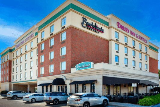 Aerial view of Drury Inn & Suites St. Louis Forest Park showcasing the multi-story hotel, a large roadside marquee sign, ample guest parking, and convenient nearby highway access.