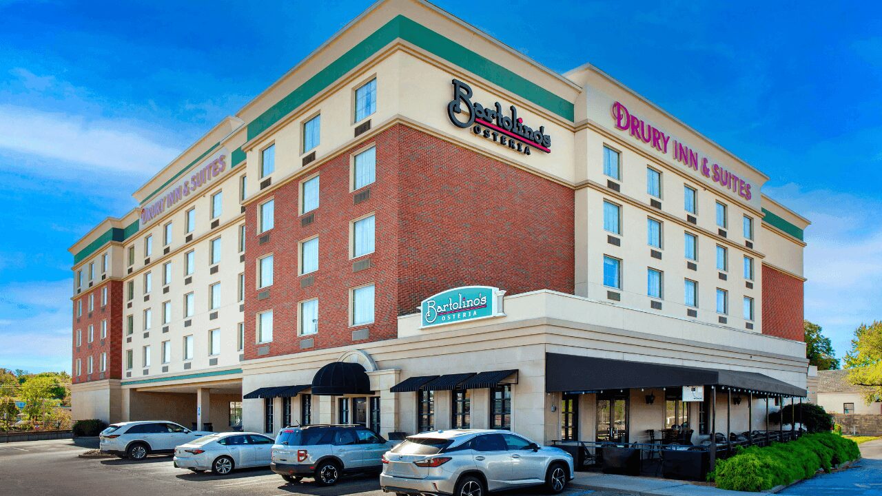 Aerial view of Drury Inn & Suites St. Louis Forest Park showcasing the multi-story hotel, a large roadside marquee sign, ample guest parking, and convenient nearby highway access.