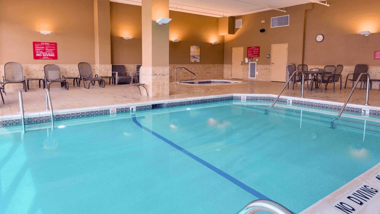 Inviting indoor swimming pool and relaxing hot tub area equipped with surrounding lounge chairs, patio tables, and accessible entry at Drury Inn & Suites St. Louis Forest Park.