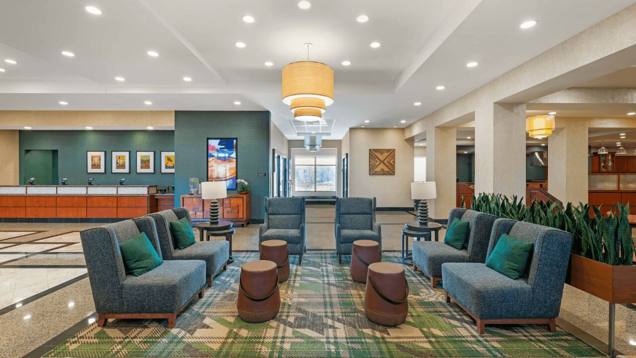 Spacious, brightly lit hotel lobby featuring a comfortable dining area with numerous tables and a hot food service counter for complimentary breakfast and evening receptions at Drury Plaza Hotel St. Louis Brentwood.