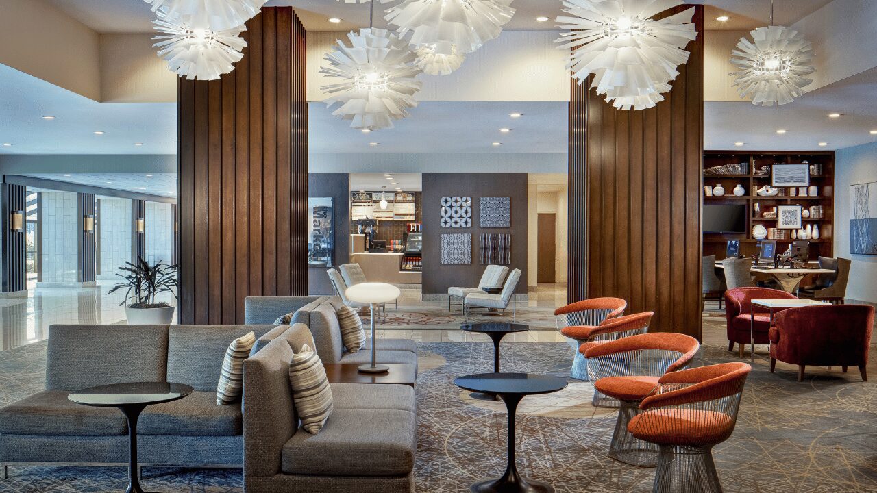 Spacious, modern lobby at the Marriott St. Louis Airport featuring a large, comfortable circular seating area, a contemporary wood-paneled ceiling, and elegant overhead lighting.