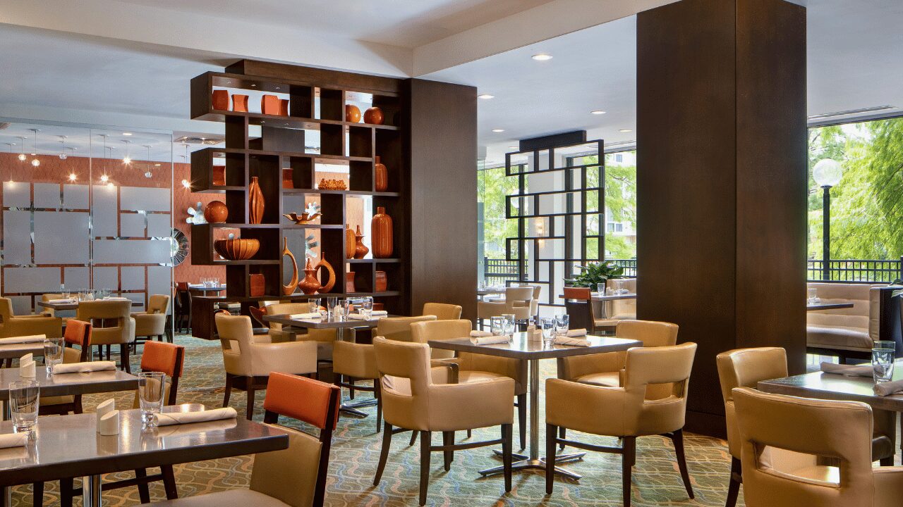 Inviting restaurant and bar area inside the Marriott St. Louis Airport, featuring modern green chairs, wooden dining tables, and flat-screen TVs above a well-lit bar counter.