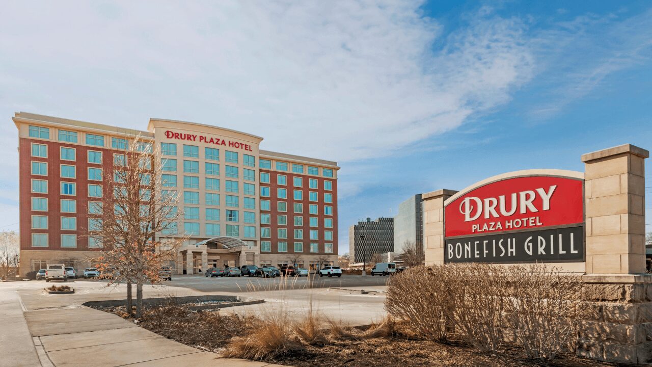 Aerial view of the modern, multi-story exterior and adjacent covered parking garage of the Drury Plaza Hotel St. Louis Brentwood on a bright, sunny day.