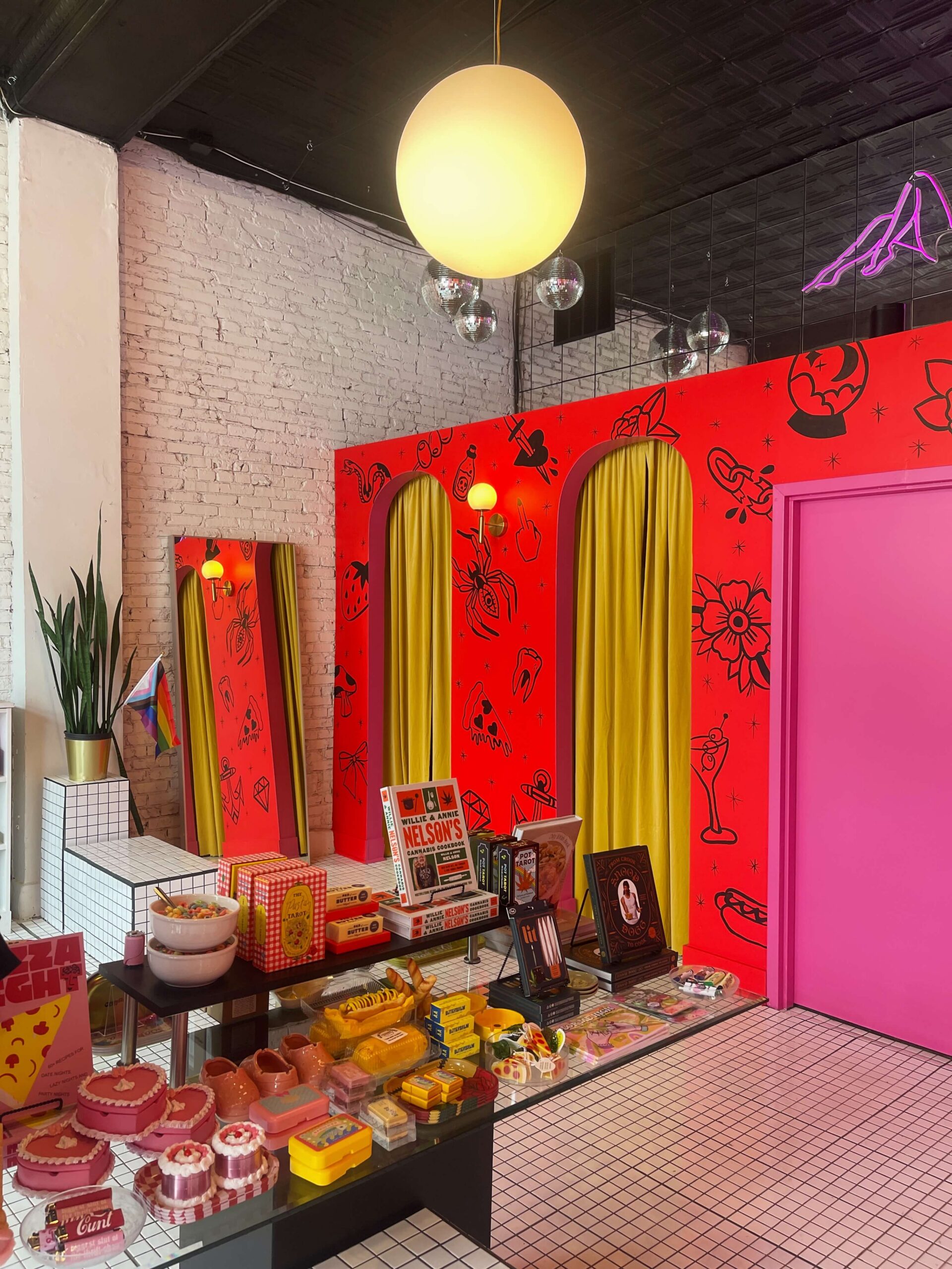 A retail display at Golden Gems featuring Willie Nelson cookbooks, colorful candles, and heart-shaped decor against a bright red illustrated wall with yellow arched curtains.