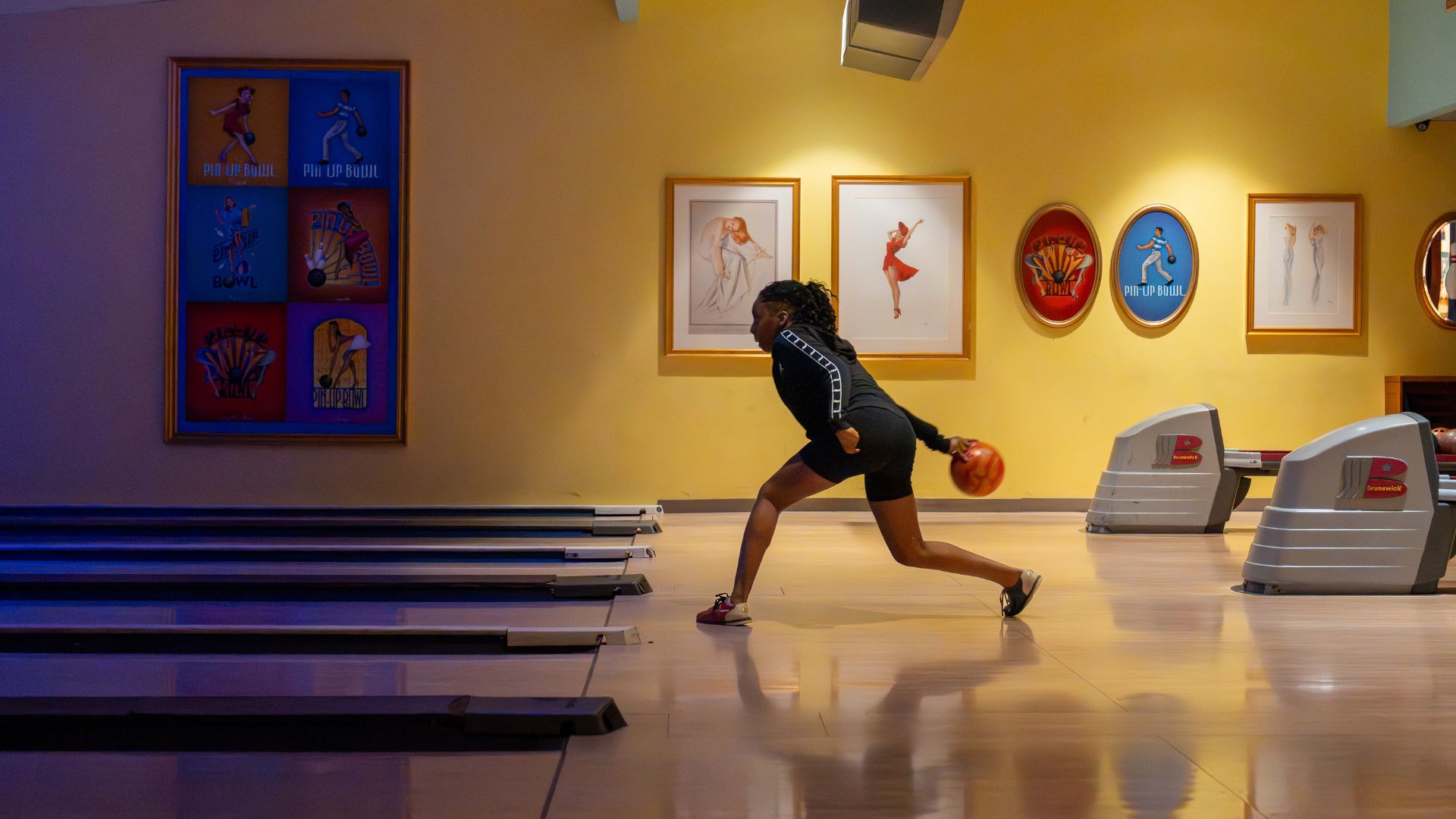 A teenage girl bowls with pin-up girl memorabilia in the background.