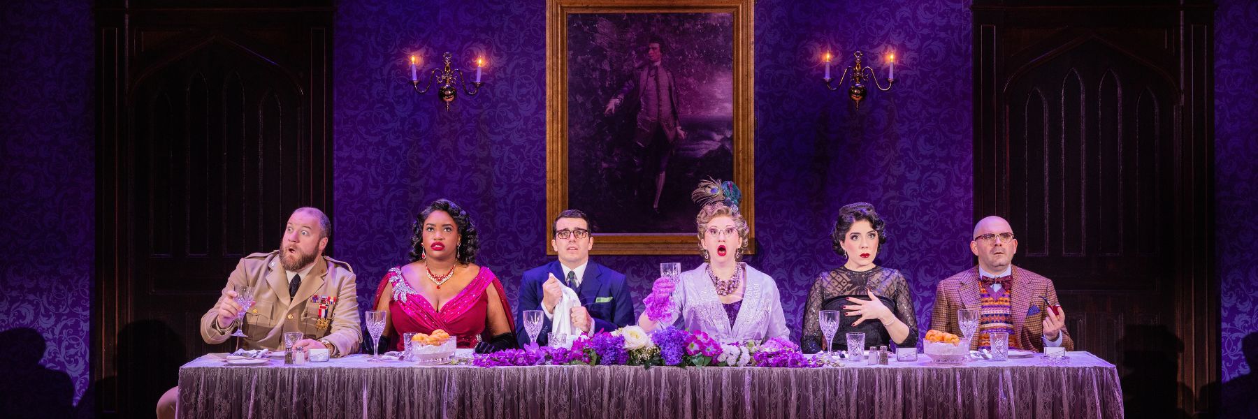 The cast of Clue sits at a long dining table as the mystery begins.
